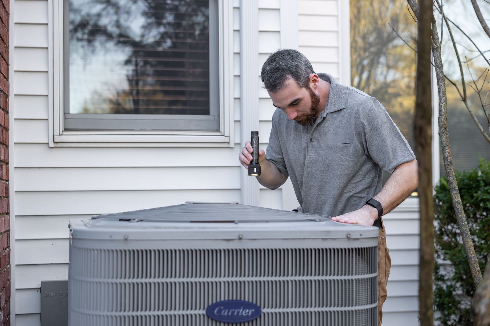 Technician inspecting an outdoor residential air conditioning unit with a flashlight