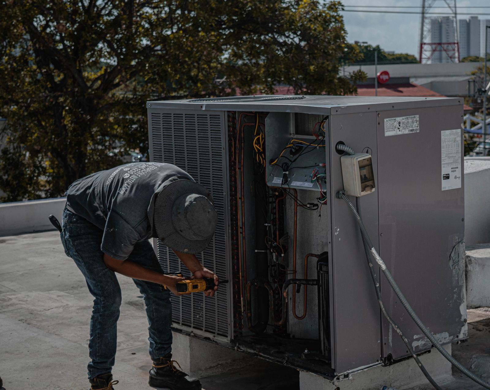Technician repairing an outdoor air conditioner condenser unit with a power drill